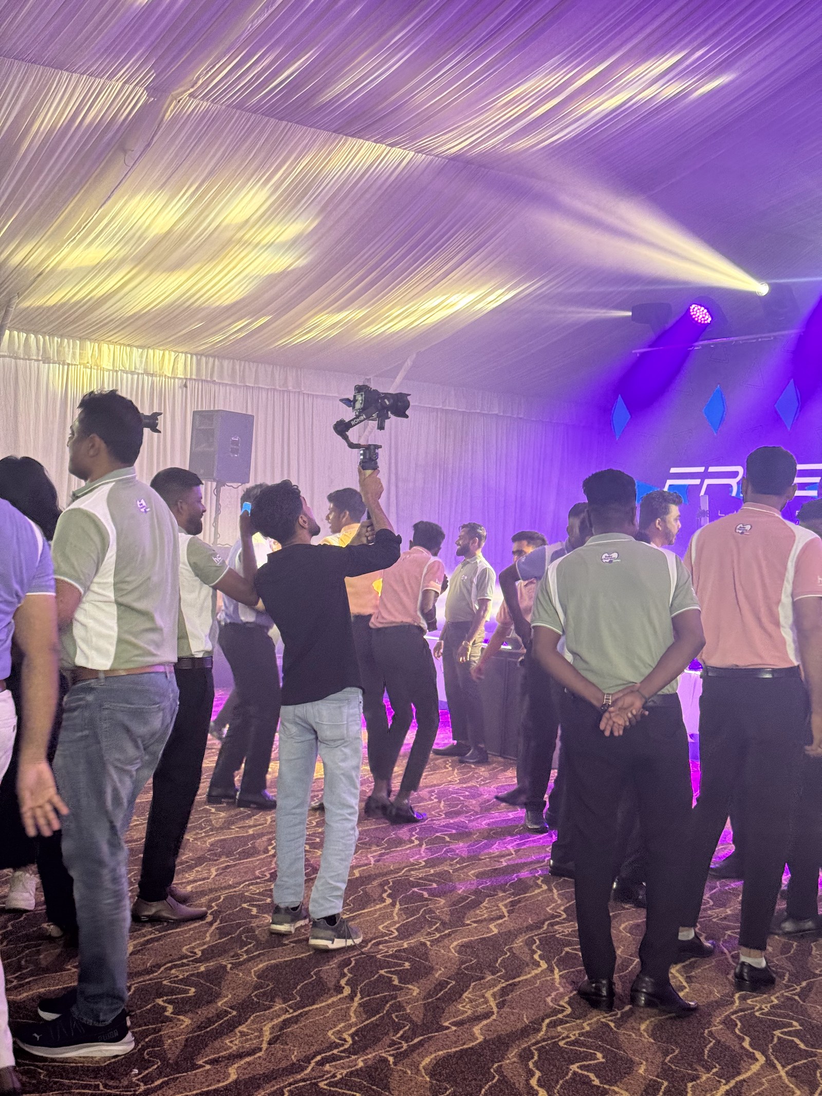 Crew and guests on the event floor under purple stage lighting